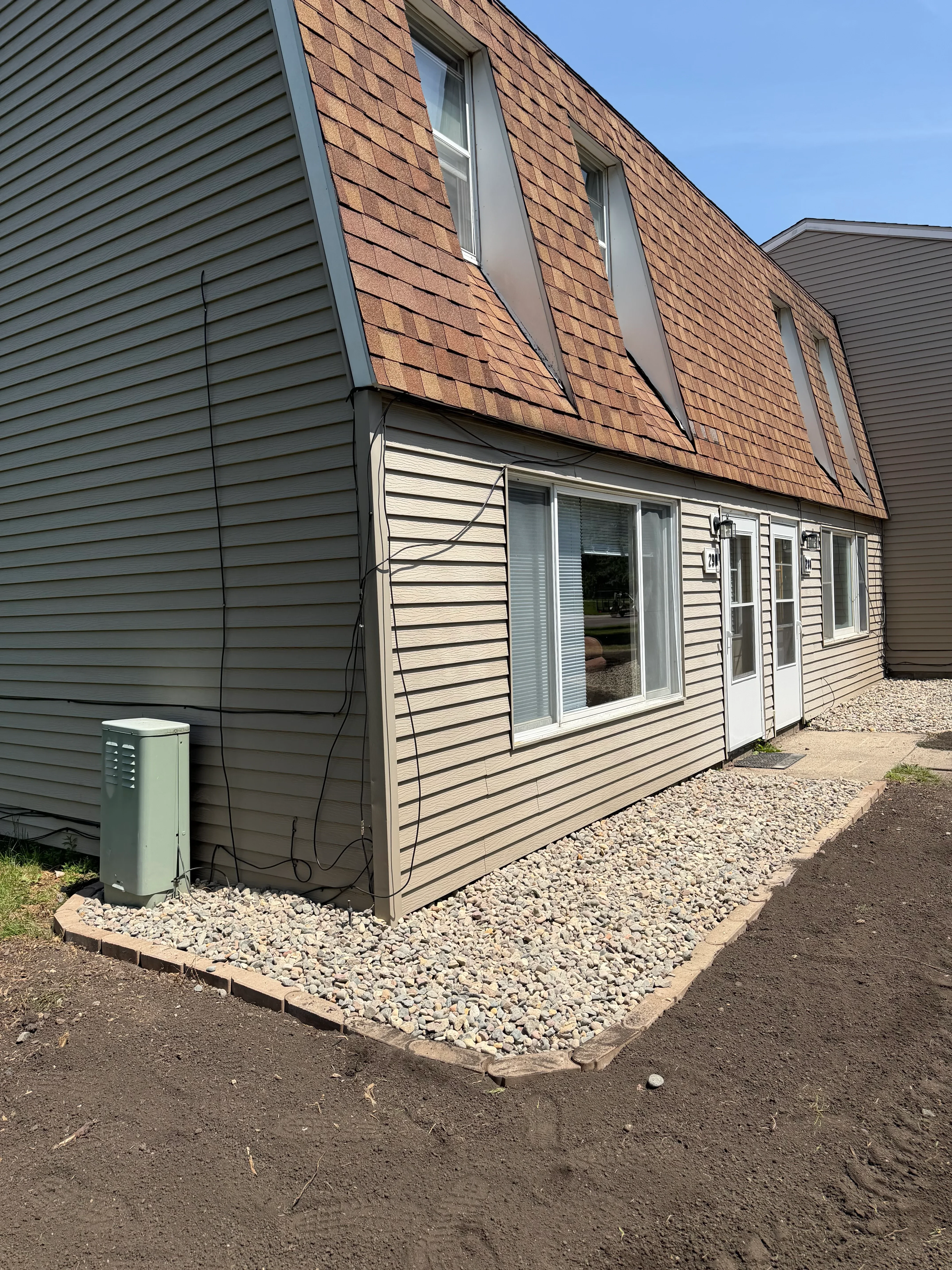 Gravel landscape bed installation with stone border along residential building foundation