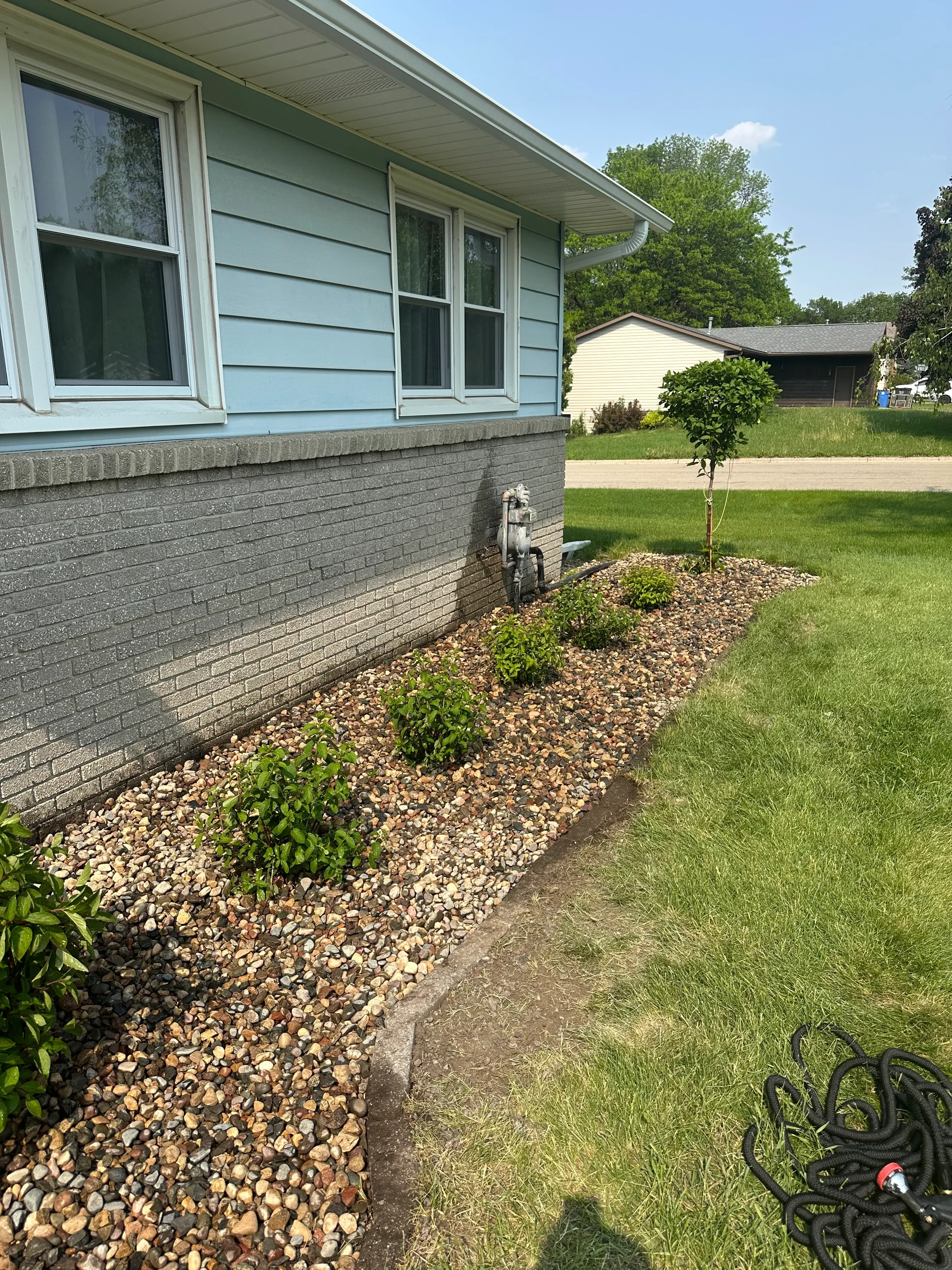 Composite deck with river rock beds, plantings, and manicured lawn in residential backyard