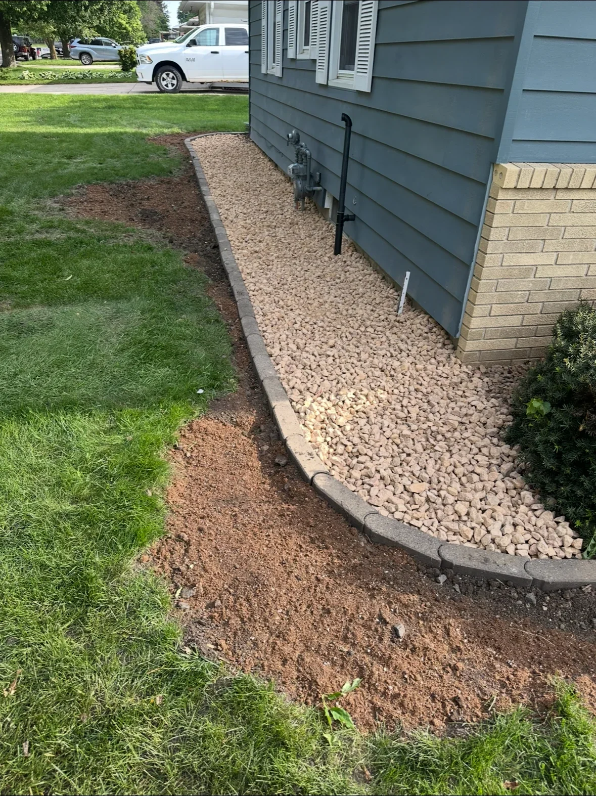 Gravel drainage bed with curved concrete edging along home foundation and gray siding