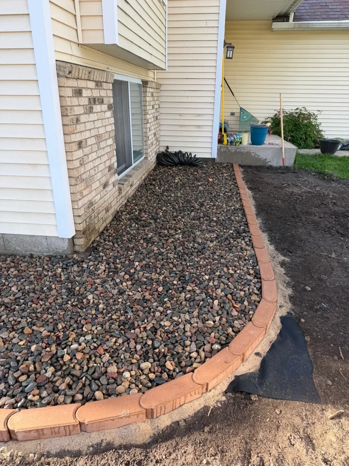 Gravel patio with curved brick edging, river rock aggregate, and landscape border installation