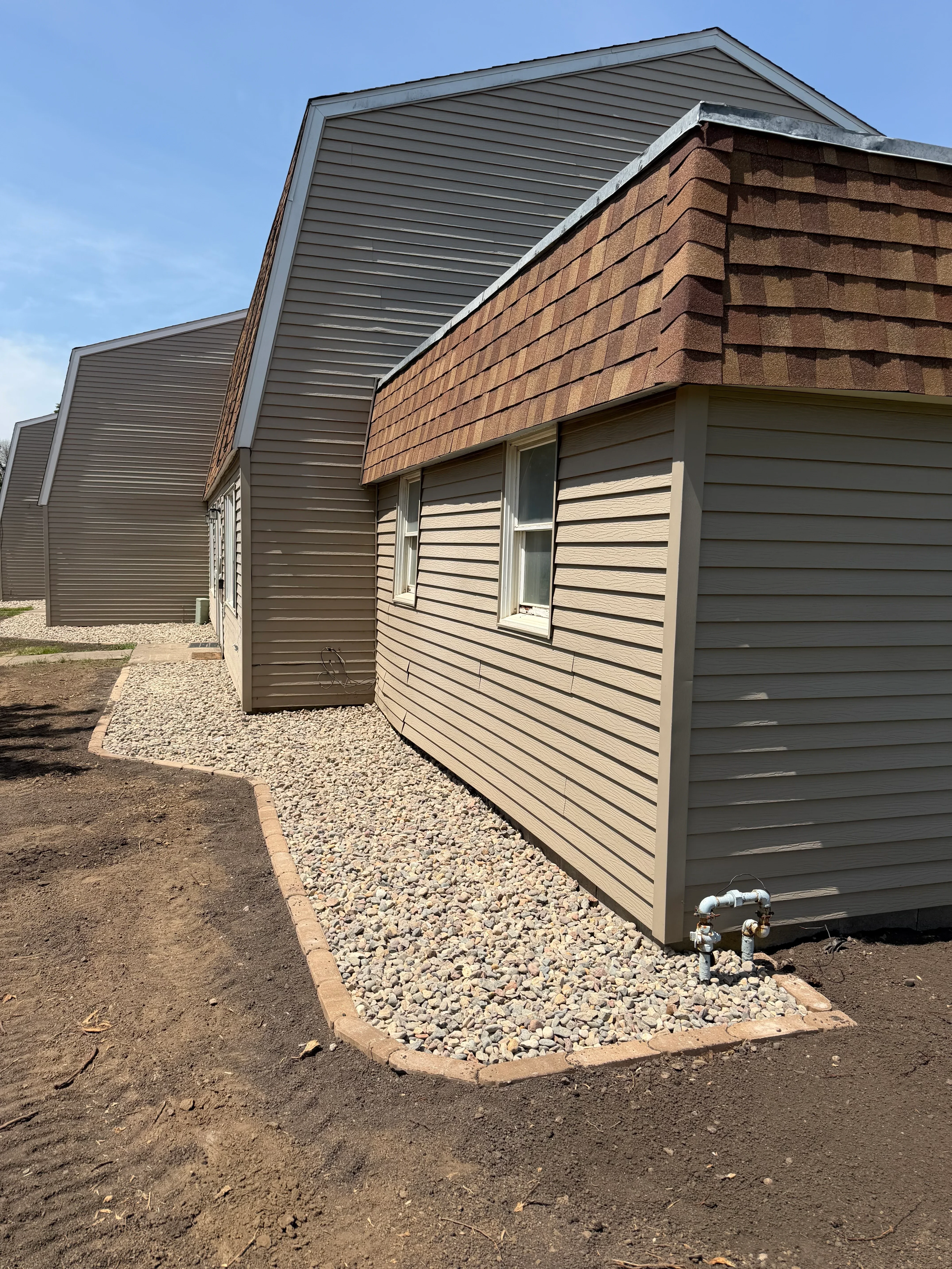Metal standing seam roof with gutters and downspout on brick building with gravel drainage base