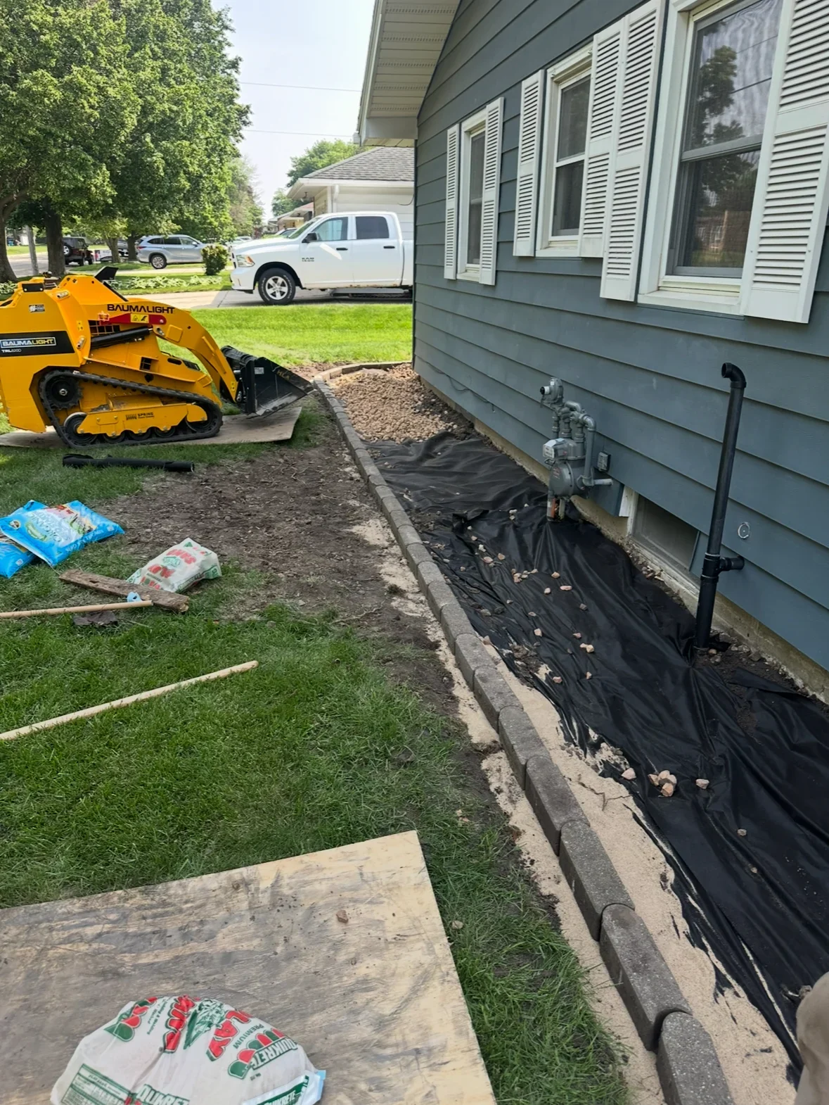 Skid steer loader, black landscape fabric, and graded soil bed at home foundation