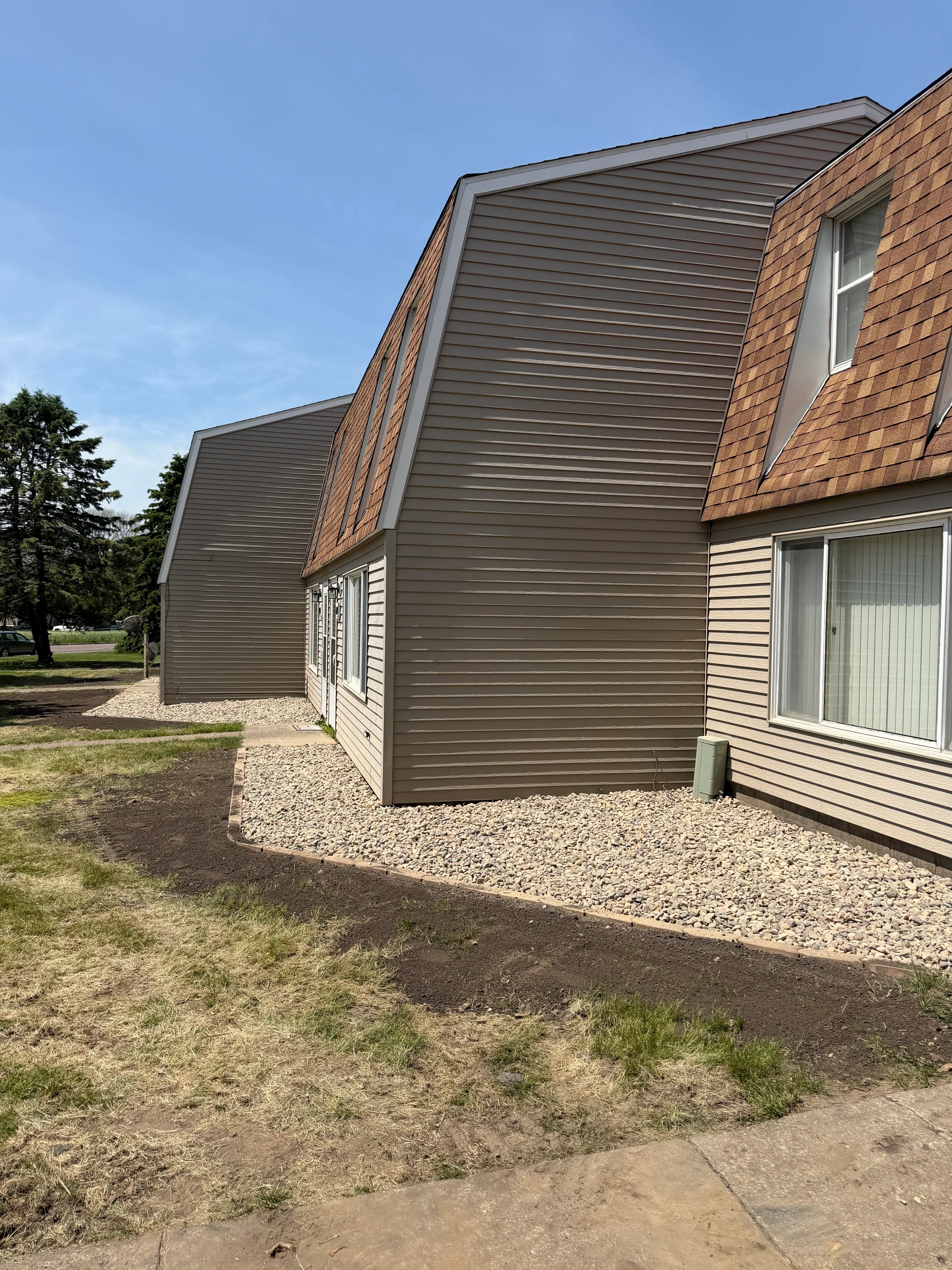 Metal carport with corrugated panels, gravel base, and stone edging on prepared ground