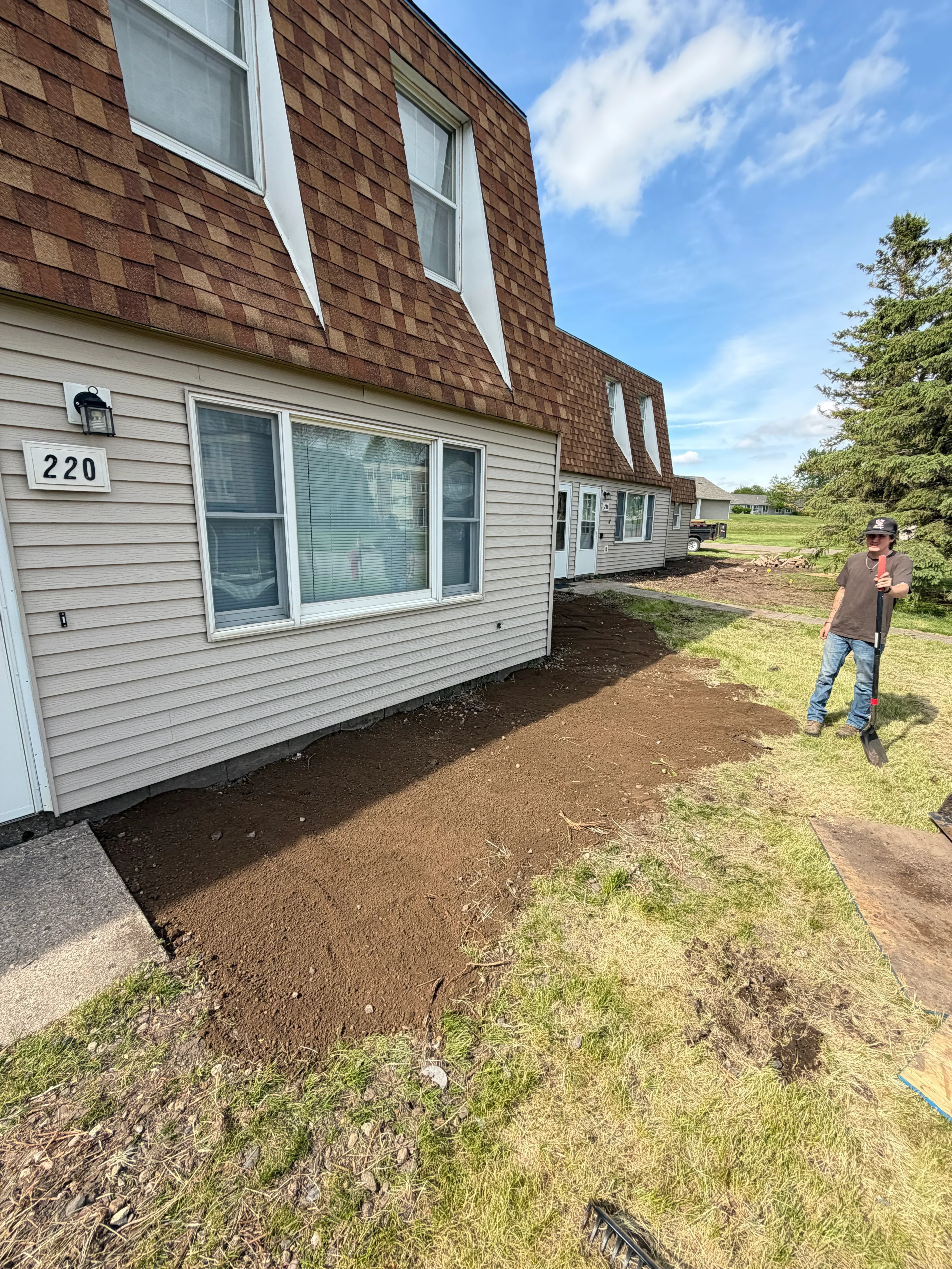 Residential grading work with sloped soil excavation and drainage preparation around home foundation
