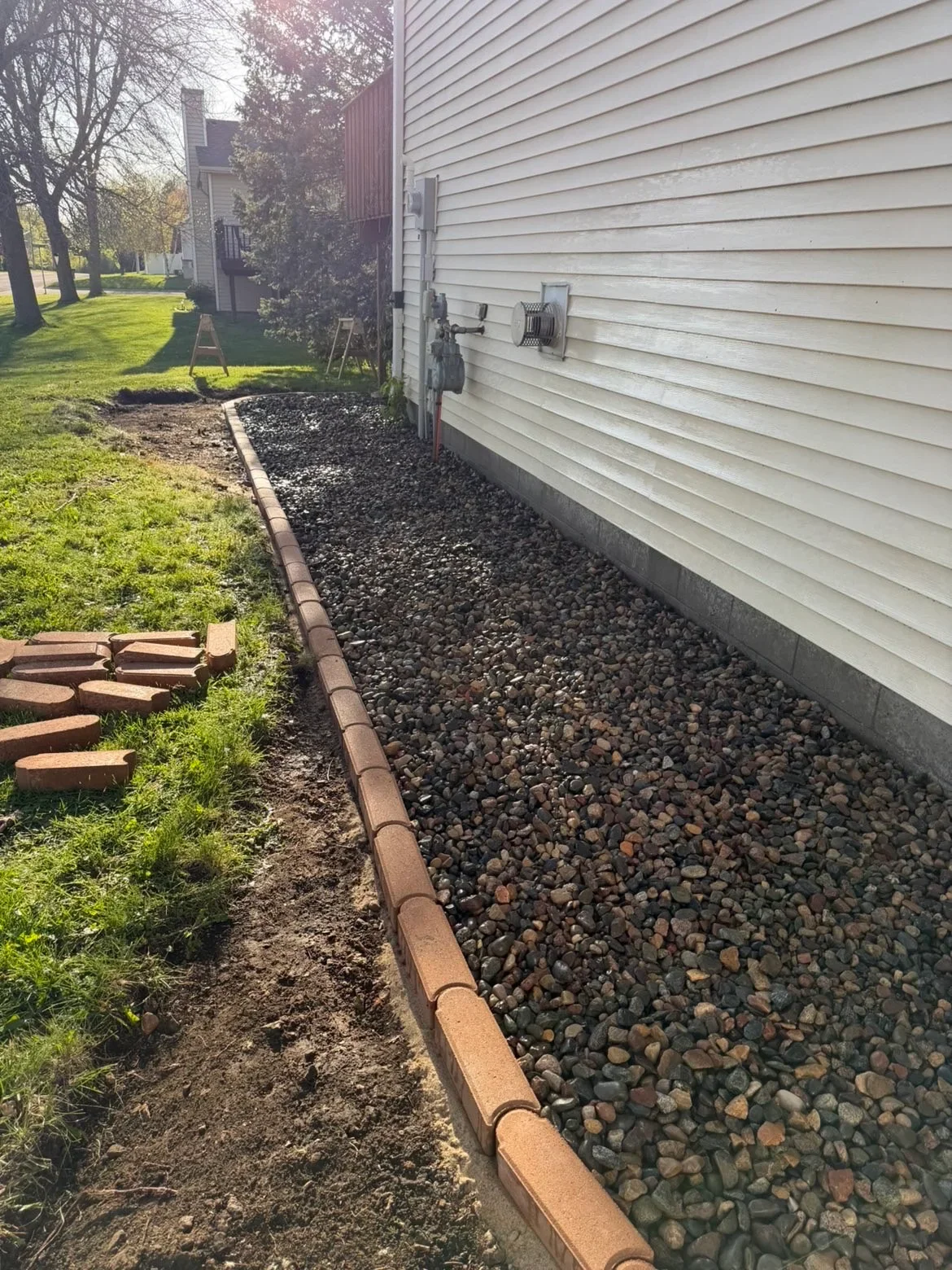 River rock drainage bed with steel edging along house foundation and vinyl siding