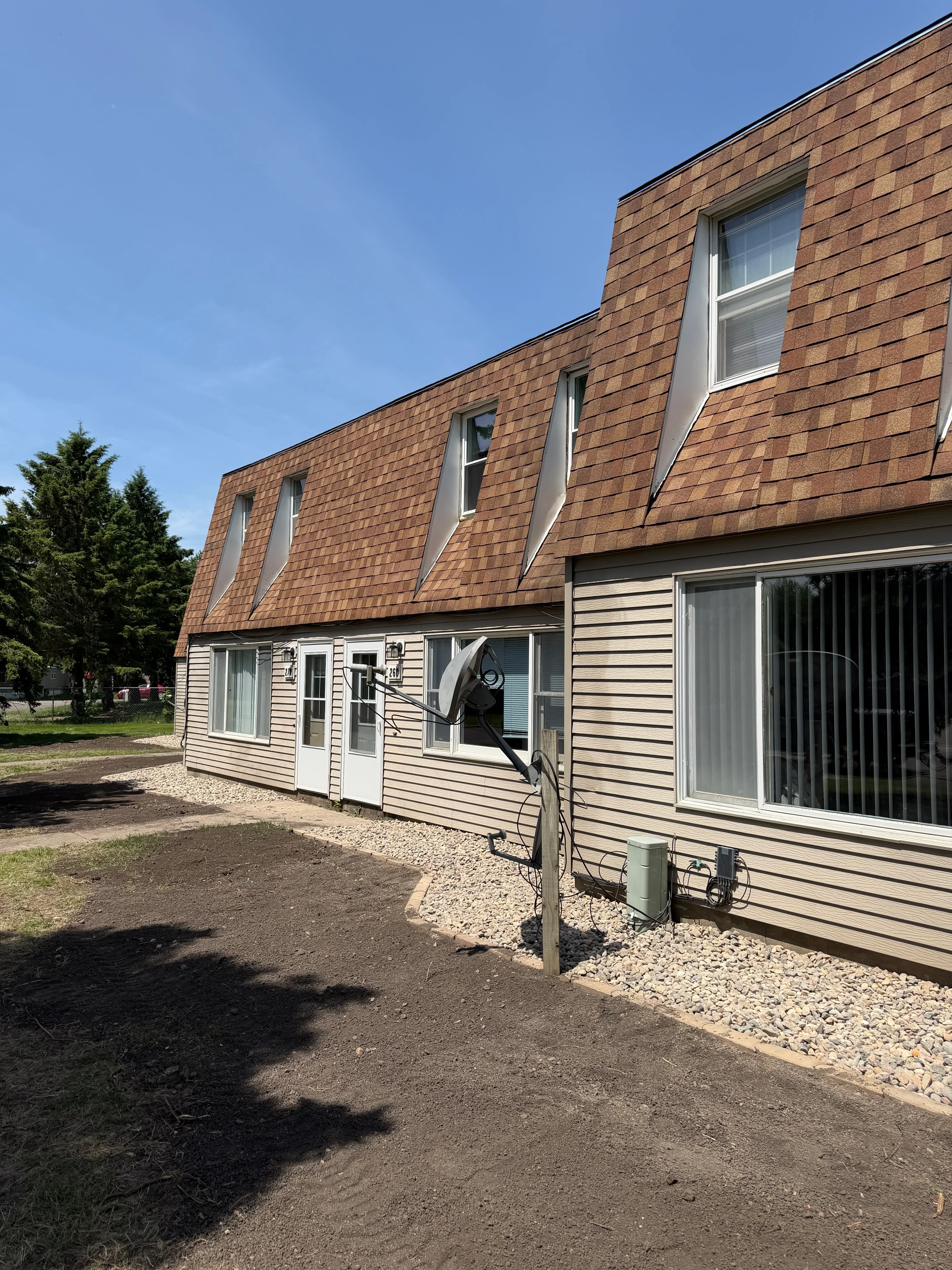 Brick residential building with corrugated metal siding, gravel landscaping, and concrete walkways