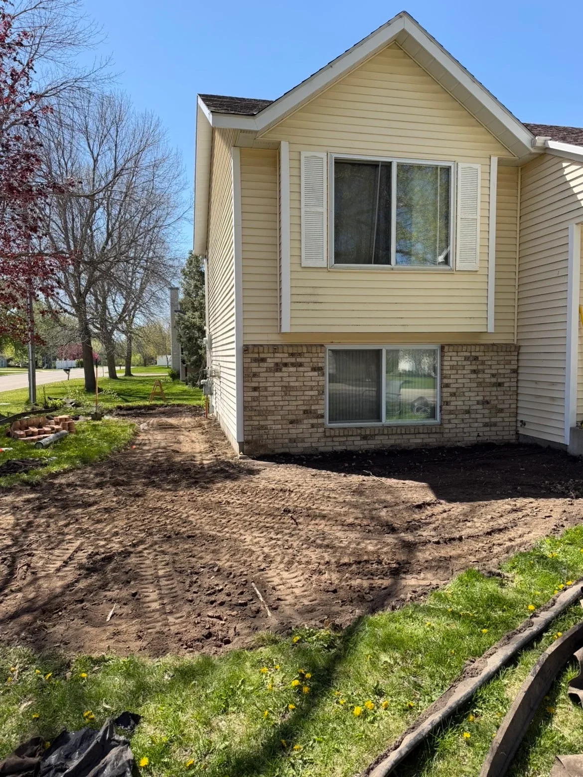 Graded front yard with exposed soil, brick foundation, vinyl siding, and landscape edging
